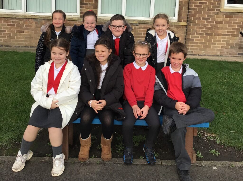 group of pupils sitting on a bench with some standing behind the